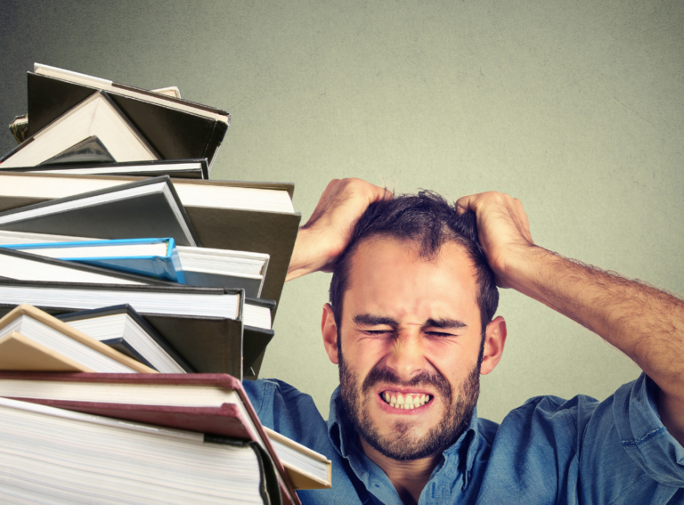 Bücherstapel, daneben verzweifelter Mann, rauft sich die Haare